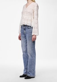 Haut en broderie anglaise blanche avec des manches évasées et un ourlet festonné, associé à un jean taille haute bleu clair et des bottines noires.