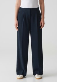 Navy wijde broek met een geplooid voorpand, op maat gemaakte snit en gladde stof. Gecombineerd met witte sneakers voor contrast.
