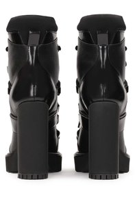 Paire de bottines noires à talons hauts avec talons épais, finition vernie et mate, vues de dos sur fond blanc.