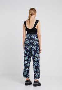 Svart linne med vit kant som är kombinerat med hög midja, vida marinblå byxor med ett färgglatt lövmönster och plattformsskor i svart.