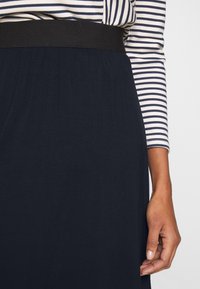 Námořnická sukně s texturovanou látkou, která má černý elastický pas. Na sukně je částečně vidět pruhovaný top s dlouhým rukávem.