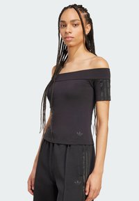 Musta olkaimeton paita lyhyillä hihoilla, jossa on teksturoituja pystysuoria raitoja hihoissa ja pieni logo helmassa.