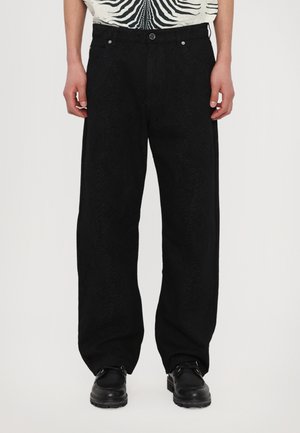 Black wide-leg pants with a textured pattern, featuring front pockets and a button closure. Styled with a patterned shirt and black shoes.