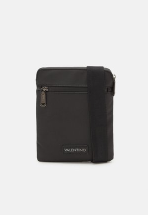 Sac bandoulière noir Valentino avec poche zippée devant et bandoulière réglable sur fond blanc uni.