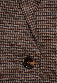 Gros plan d’un tissu à motif pied-de-poule marron et marine avec un bouton marbré foncé sur un manteau ou une veste.