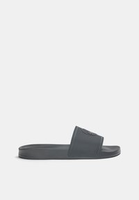 Mörkgrå slide-sandal i texturerad gummi med en platt sula. Har ett brett band och en rund logotypaccent på bandet.