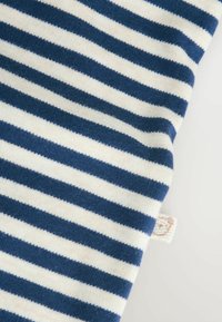 Tessuto di cotone con righe orizzontali blu navy e crema. Texture morbida con un'etichetta visibile nell'angolo in basso a destra.