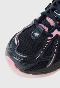 Tige en maille noire texturée avec des accents roses, protection renforcée au niveau des orteils et semelle rembourrée. Présente un logo et des lignes de design détaillées.