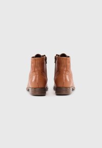 Bottes chelsea en cuir marron avec une texture lisse, des fermetures éclair latérales et des talons en bois empilés. Bout arrondi et détails de couture minimaux.