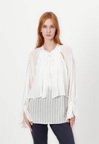 Blusa bianca con una vestibilità ampia, caratterizzata da un colletto con fiocco, maniche a campana e tessuto trasparente con delicate striature.