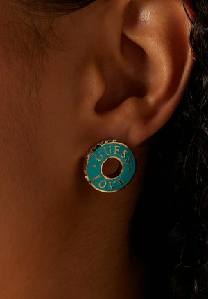 Turkooise cirkelvormige oorbellen met de tekst "GUESS LOVE"; gouden accenten en een centrale open cirkel; getextureerd oppervlak voor visuele aantrekkingskracht.
