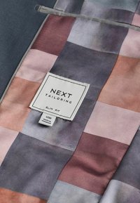 Maßgeschneiderter Jackeninnenteil mit einem mehrfarbigen Karomuster in Pastelltönen. Mit einem Etikett, das "NEXT TAILORING SLIM FIT" liest.