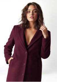 Blazer bordeaux con colletto a revers, chiusura con un solo bottone e tasche laterali. Tessuto liscio e vestibilità sartoriale.