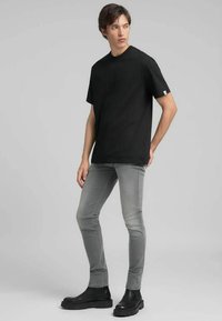 T-shirt nera in cotone con scollo rotondo e maniche corte, abbinata a jeans grigi aderenti e stivaletti neri alla caviglia. Design semplice e lineare.