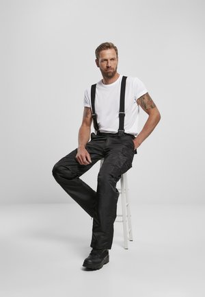 Svarta cargobyxor med hängslen, tillverkade av ett glatt material. Har fickor och en avslappnad passform. Kombineras med en enkel vit t-shirt och svarta kängor.