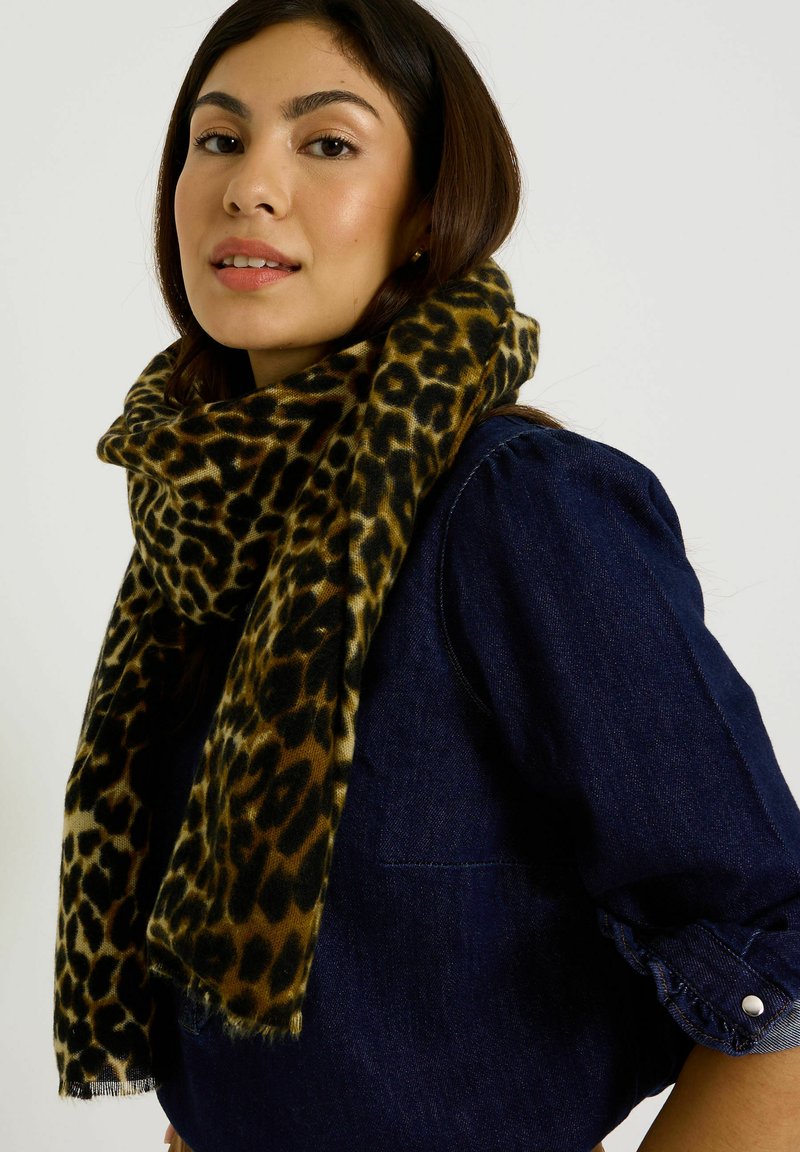 Écharpe en imprimé léopard en tissu doux, présentant des tons chauds de marron et de noir, drapée autour du cou, associée à un haut en denim foncé.