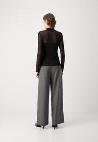 Maglietta nera a maniche lunghe con tessuto trasparente sulle spalle, abbinata a pantaloni larghi grigi a vita alta, caratterizzati da una texture liscia.