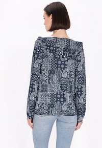 Giacca con cappuccio blu navy con motivi paisley e geometrici bianchi; maniche lunghe, vestibilità comoda e texture del tessuto liscia.