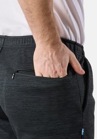 Schwarze Jogginghosen mit strukturiertem Muster, ausgestattet mit einer seitlichen Reißverschlusstasche und elastischem Bund. Ein kleiner blauer und gelber Akzent ist sichtbar.
