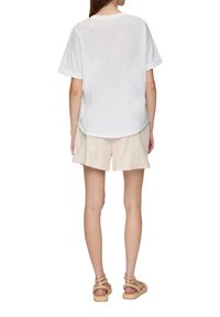 Witte katoenen t-shirt met opgerolde korte mouwen, relaxte pasvorm en afgeronde zoom. Gepaard met beige gestreepte shorts en beige sandalen.