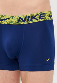Mørkeblå herreboxere med et gult og grønt mønstret elastikbånd, der pryder stort "NIKE" tekst og en lille gul Nike swoosh på benet.