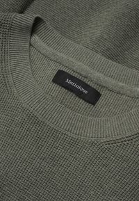 Pull en maille vert olive avec un motif texturé, doté d'un col côtelé et d'une étiquette en tissu portant le nom "Matinique" en texte blanc.