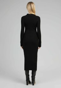 Robe noire en tricot côtelé avec de longues manches, un col discret et une longueur midi, associée à des bottes noires montantes.