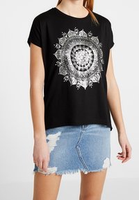 Svart bomulls-t-shirt med kort ärm, med en silver mandala design på framsidan; parat med en slitna denim minikjol.