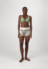 Light green ribbed bikini top paired with cream lace shorts featuring a crochet design and drawstring waistband. Model stands barefoot.