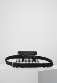 Borsa in tessuto a scacchi bianco e nero con una strap in pelle nera e una fibbia. Presenta una chiusura a pattina e due accenti verticali in pelle.