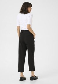 Zwarte hoge taillebroek met een relaxte fit, zijzakken en achterpanddetails. Gecombineerd met een aansluitend wit T-shirt met korte mouwen en glanzende loafers.