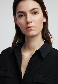 Camicia nera con bottoni e colletto, caratterizzata da una morbida texture e due tasche sul petto. Il design è semplice e classico, adatto per un look casual.
