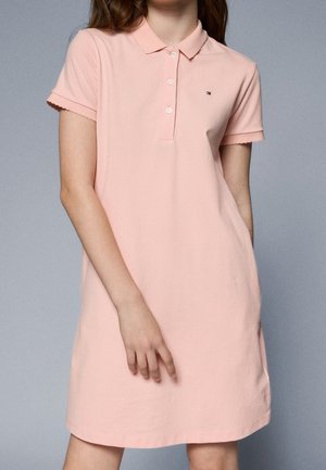 Robe polo en coton rose clair avec un col à volants et des manches courtes. Dotée d'une patte de boutonnage à trois boutons et d'un petit logo sur la poitrine.