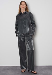 Completo drappeggiato con una camicia grigia metallica con chiusura a bottoni e pantaloni larghi coordinati, entrambi in un materiale elegante e liscio.