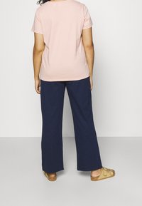 T-shirt rosa chiaro a maniche corte con scollo rotondo, abbinato a pantaloni larghi blu navy e sandali beige.