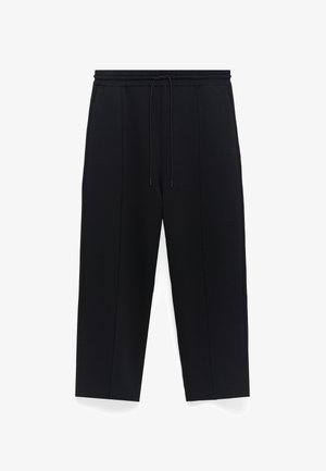 Czarne spodnie o luźnym kroju, z elastycznym paskiem z sznurkiem oraz bocznymi szwami biegnącymi wzdłuż nogawek. Gładka tekstura materiału.