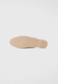 Beiger Schuhsohle mit strukturierten Grip-Mustern. Verfügt über einen flachen Absatz und eine glatte Oberfläche. Markenkennzeichnungen sind in der Mitte sichtbar.