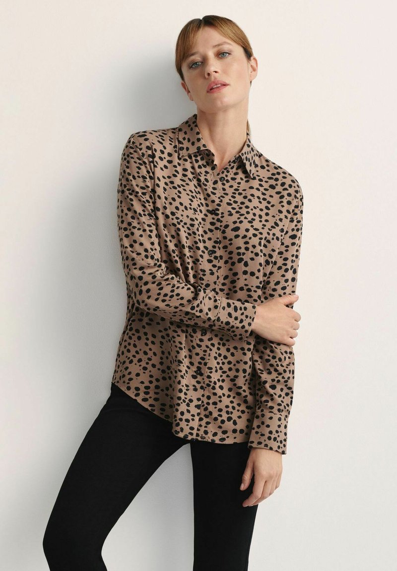 Brązowa koszula zapinana na guziki z czarnym wzorem w panterkę, długie rękawy, kołnierzyk oraz gładki, lekki materiał. Połączona z czarnymi spodniami.