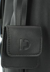 Schwarze Ledertasche mit strukturiertem Finish, ausgestattet mit einer kleinen Frontklappe, die mit einem Buchstaben 'C' geprägt ist. Verstellbarer Tragegurt ist enthalten.
