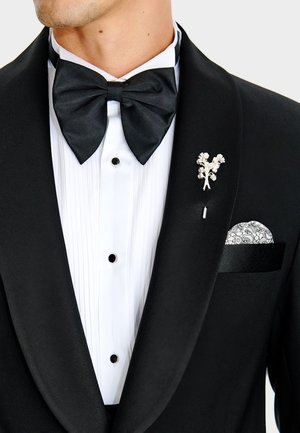 Mężczyzna w czarnym fraku z satynowym wyłogiem, białej plisowanej koszuli, czarnej muszce, kwiatowej przypince oraz wzorzystej poszetce.
