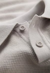 Svetle šedé polo tričko vyrobené z texturované látky s límečkem, se dvěma knoflíky na výstřihu a tkaným vzorem.