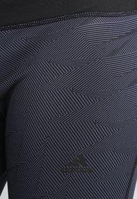 Czarne legginsy sportowe z geometrycznym wzorem w ciemnym niebieskim kolorze, wykonane z elastycznego materiału, z logo adidas na dolnej części nogawki.