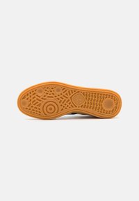Sole of a sneaker, featuring a textured rubber design in orange, with circular and linear patterns for traction.