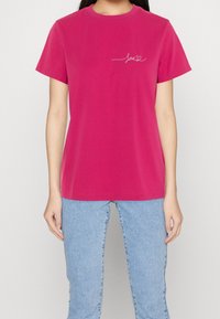 Fuchsia cotton t-shirt with short sleeves, round neckline, featuring a white cursive "love" design on the left chest area.