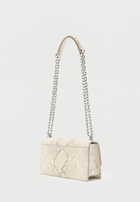 Μικρή ορθογώνια μπεζ τσάντα χειρός με σχέδιο από φίδι και μακριά αλυσίδα σε ασημί χρώμα μπροστά σε απλό φόντο.