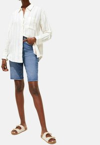 Hvidstribet skjorte med knapper, blå denimshorts og beige sandaler med stropper. Skjorten har en lomme og en afslappet pasform.