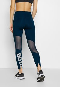 Laivastonväriset legginsit, joissa on verkkopaneelit, korkea vyötärö ja sivuventtiilit. Vasemmassa jalassa on rohkea valkoiset "DO"-teksti. Sujuva pinta.