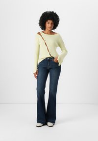 Ribbed light yellow long-sleeve top with side button detailing, paired with dark blue flared jeans and white ankle boots.