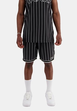 Black tank top with white stripes and large lettering, paired with matching black shorts featuring white accents and a slim fit. White sneakers.