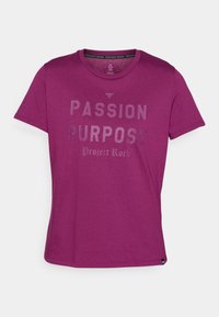 Krátký rukáv, tričko s kulatým výstřihem v živé magentové barvě s hladkým povrchem. Obsahuje výrazný, reflexní text: "PASSION PURPOSE Project Rock."